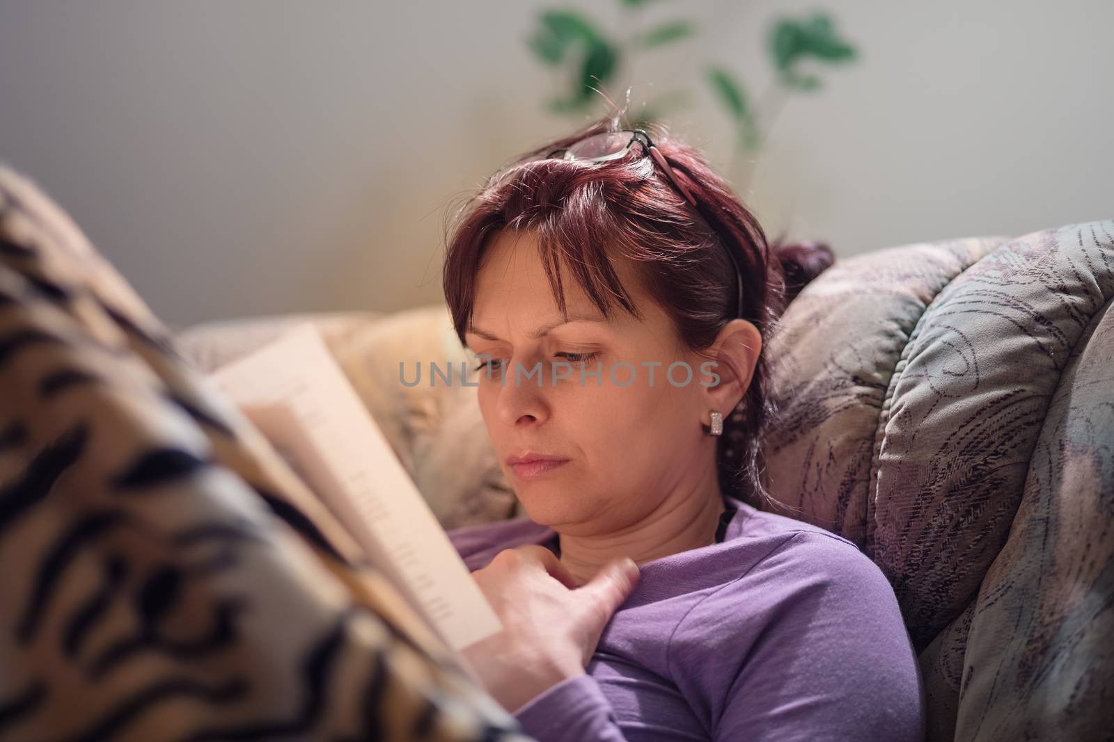 middle-aged woman is reading a book at home with the lamp on. Authentic photo, real people in real situation