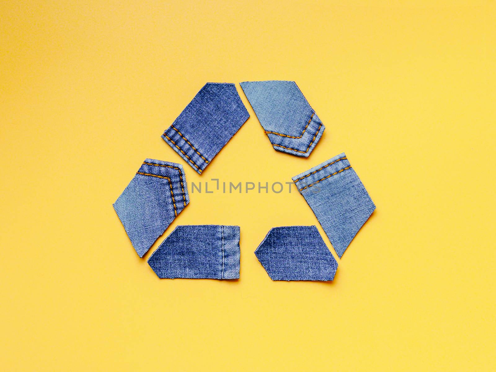 Reuse, reduce, recycle concept background. Recycle symbol made from old jeans on yellow background. Top view or flat lay.