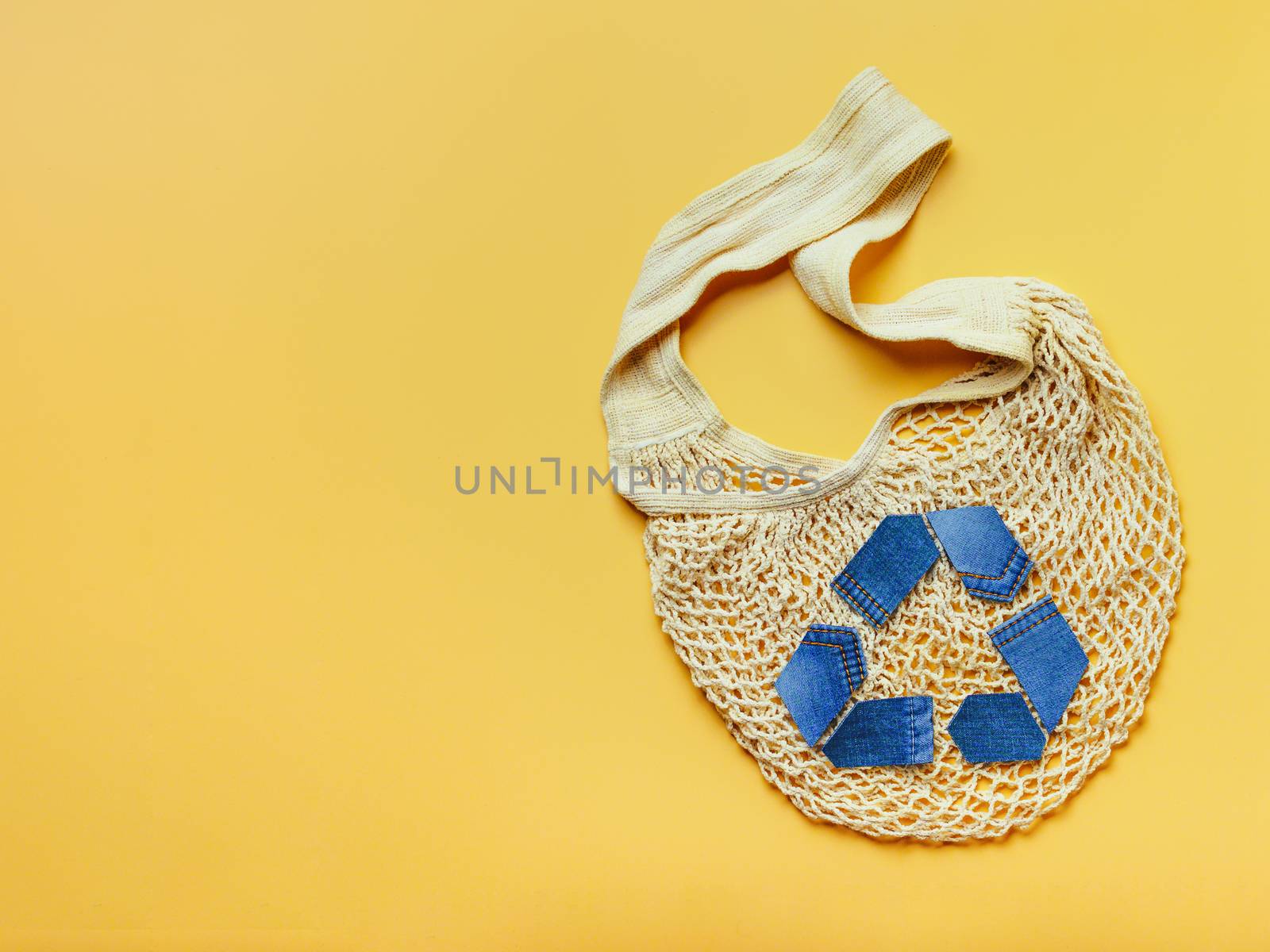 Reuse, reduce, recycle concept background. Recycle symbol made from old jeans and mesh bag on yellow background. Top view or flat lay. Copy space for text or design