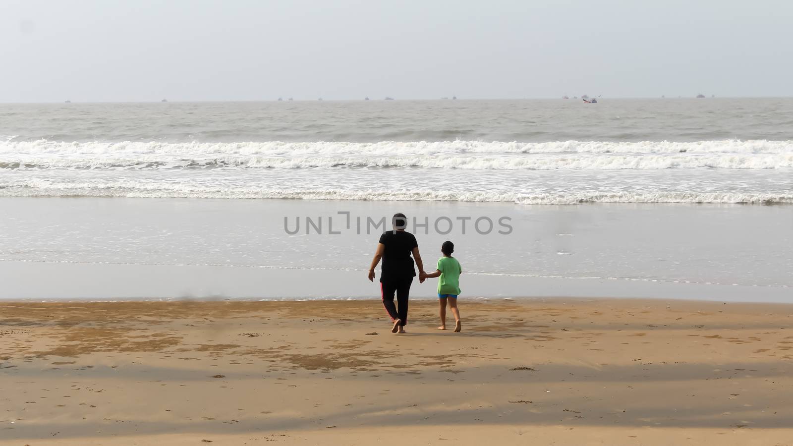 Rear View of Mother and son walking on a tropical beach in evening during sunset. The child admires his mom,s faith. Happy Mother’s day background concept. Goa, India, South Asia Pacific In Summer.