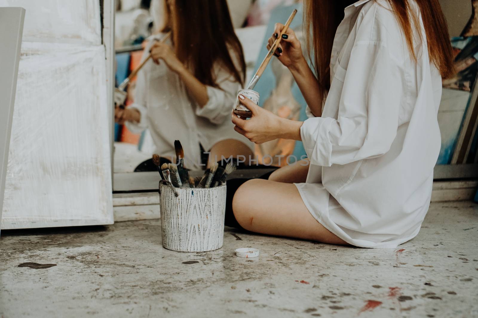 Woman painter sitting on the floor in front of mirror. Art studio interior by natali_brill