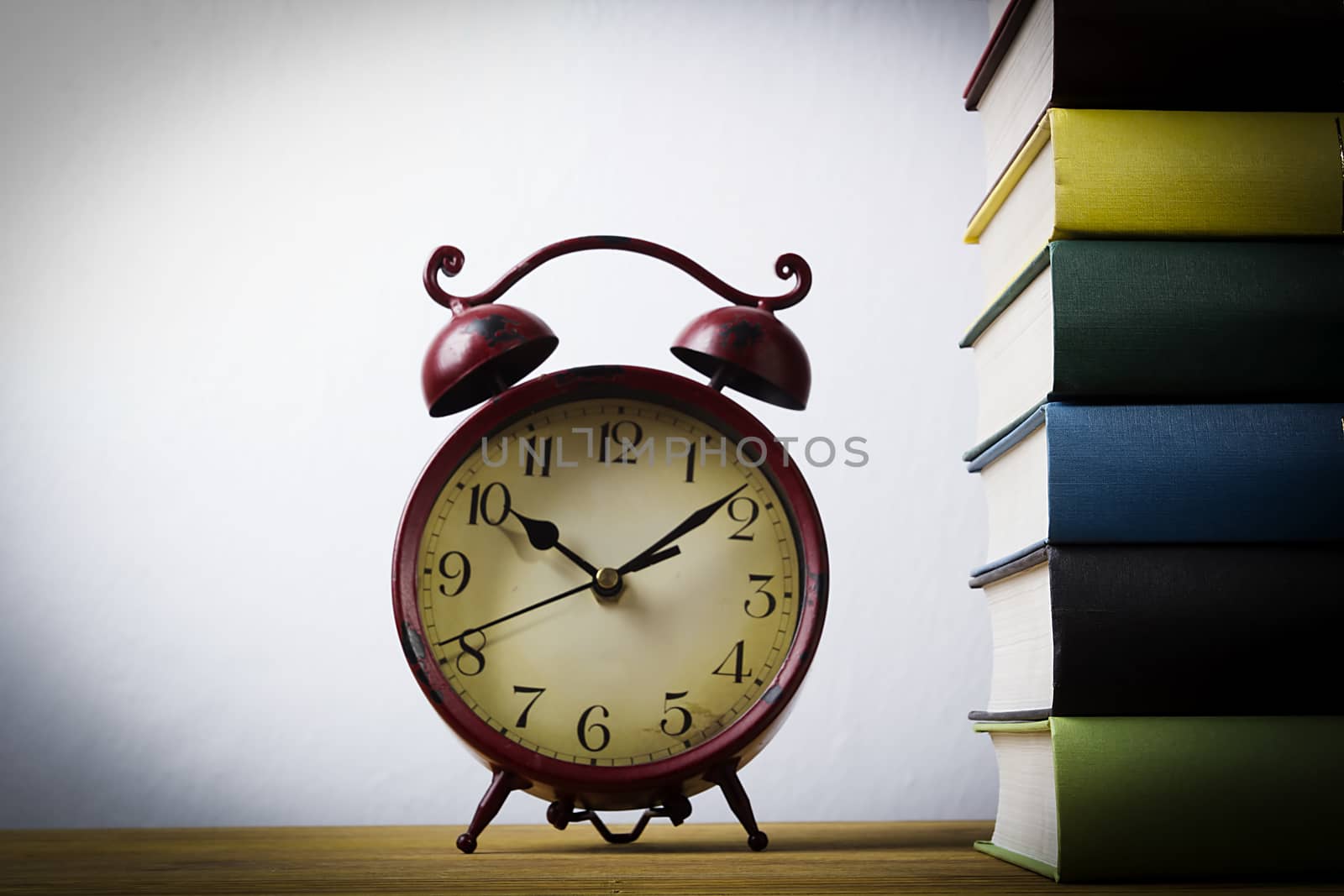 Stack of books and an alarm clock on a wooden table