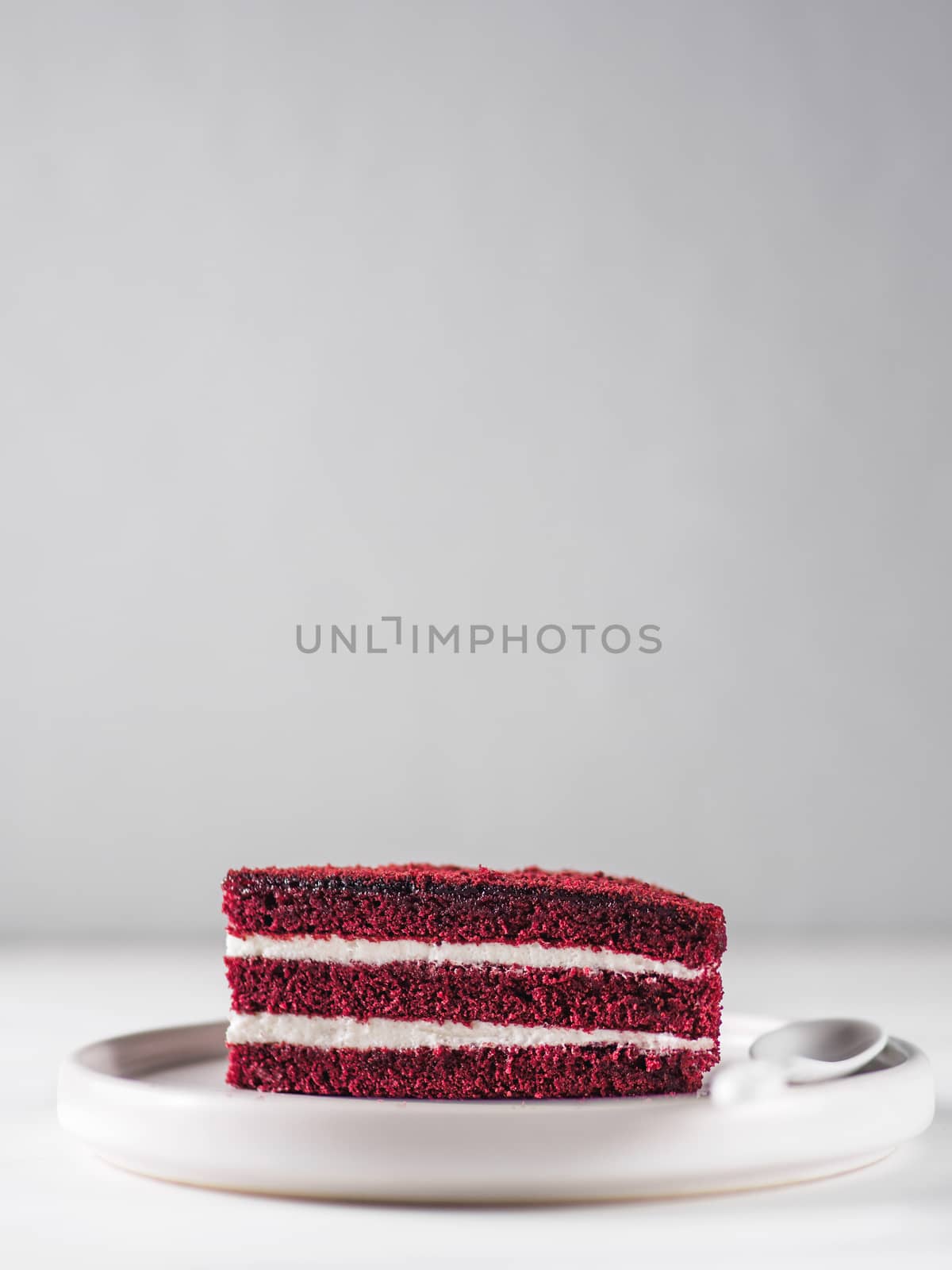 Piece of red velvet cake with perfect texture in matte plate on white marble tabletop. Slice of delicious homemade red velvet cake with raspberry and chocolate. Copy space for text.
