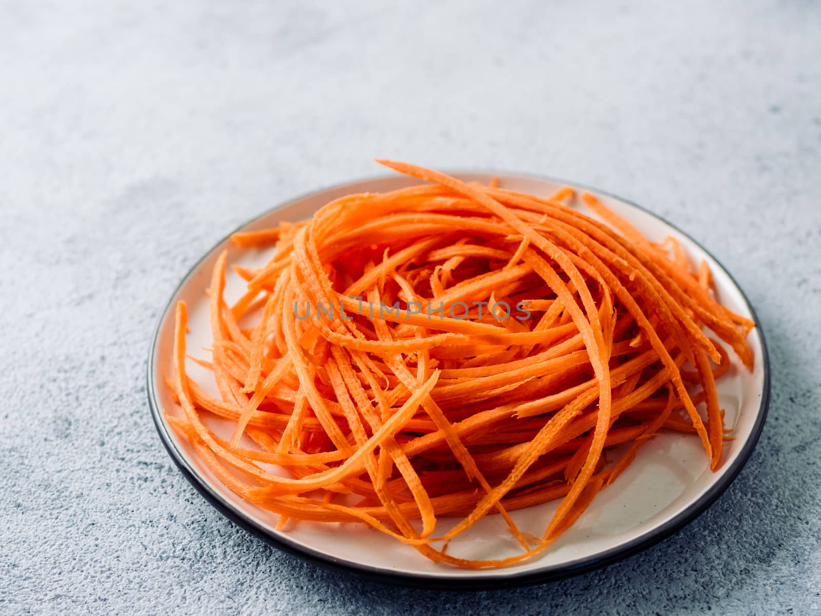 Carrot noodles on plate. Vegetable noodles - orange sweet carrot spaghetti on plate over gray cement background. Clean eating, raw vegetarian food concept. Copy space for text.