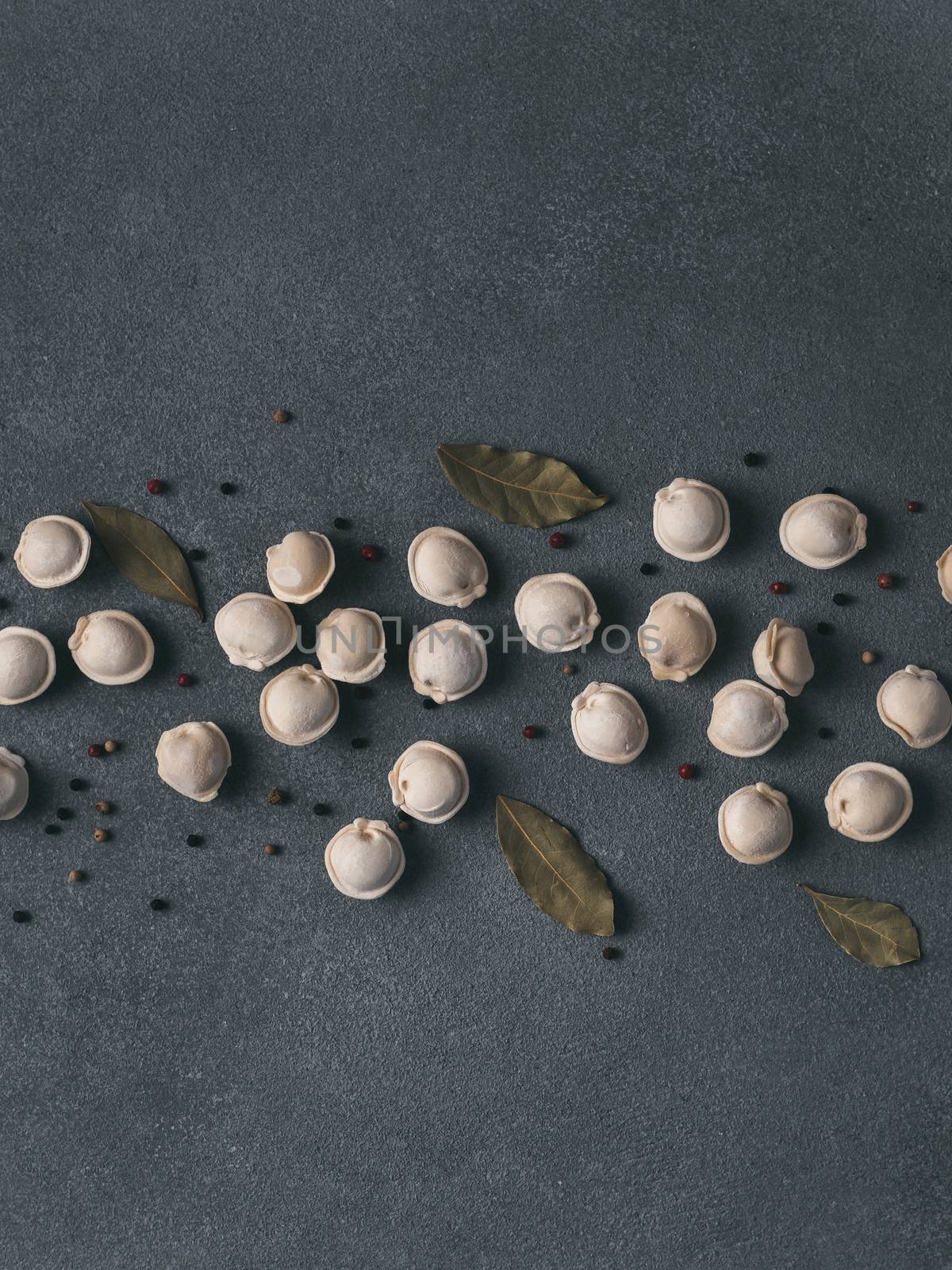 Pattern of frozen uncooked russian pelmeni with peppercorns and bay leaves on black background. Creative layout of dumplings. Beautiful scattered raw dumplings. Top view, flat lay. Copy space for text