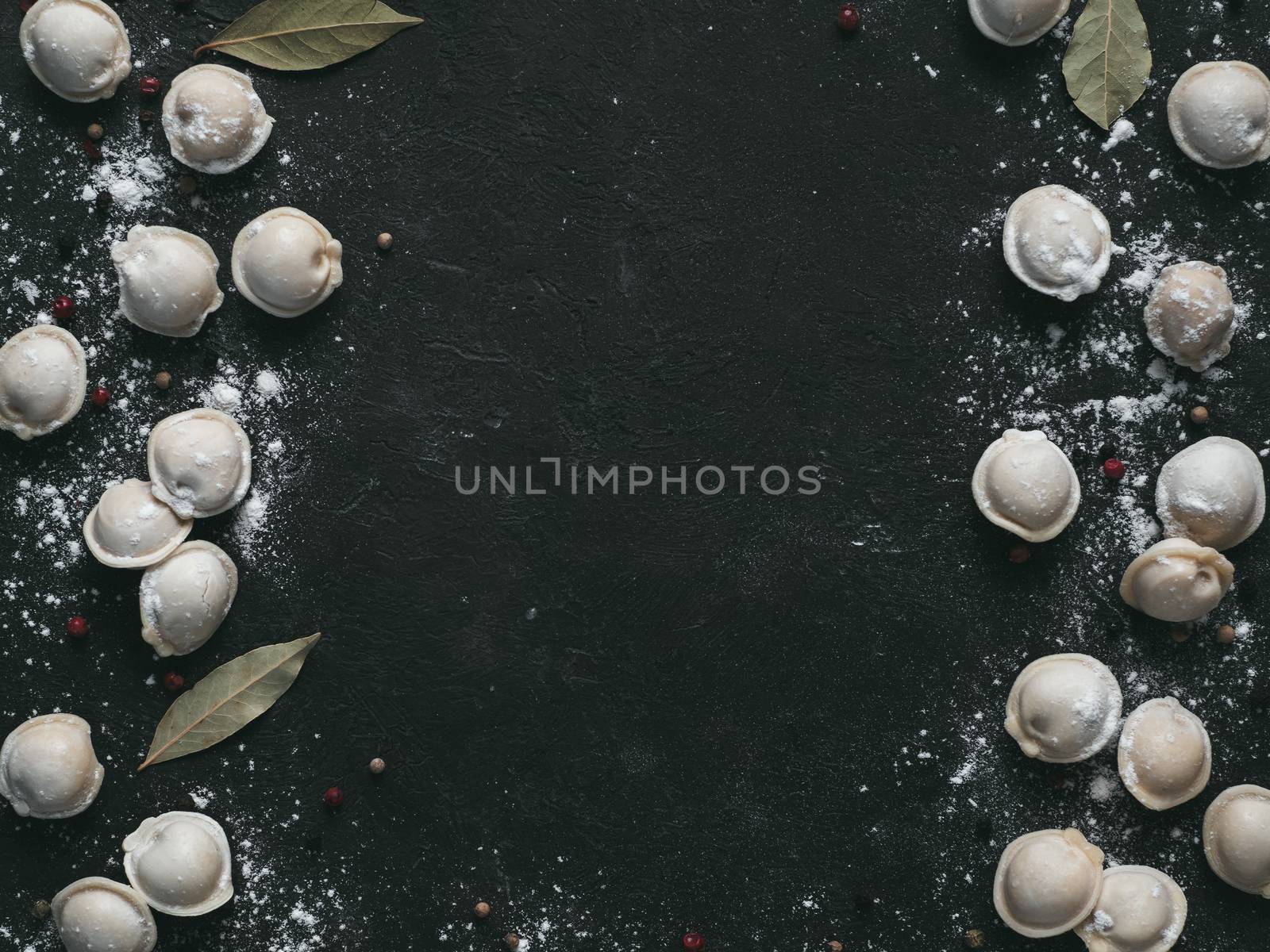 Pattern of frozen uncooked russian pelmeni with peppercorns and bay leaves on black background. Creative layout of dumplings. Beautiful scattered raw dumplings. Top view, flat lay. Copy space for text