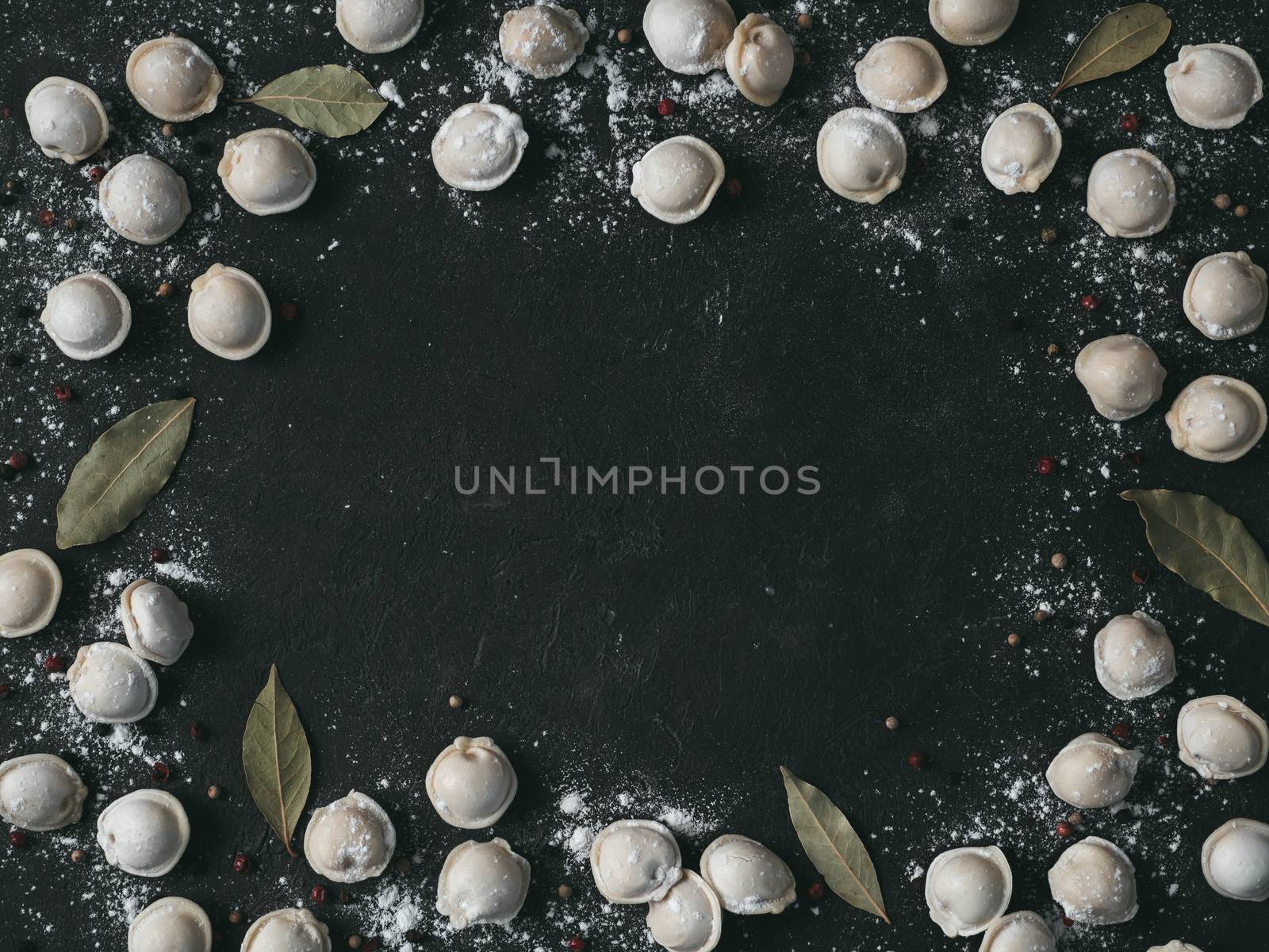 Pattern of frozen uncooked russian pelmeni with peppercorns and bay leaves on black background. Creative layout of dumplings. Beautiful scattered raw dumplings. Top view, flat lay. Copy space for text