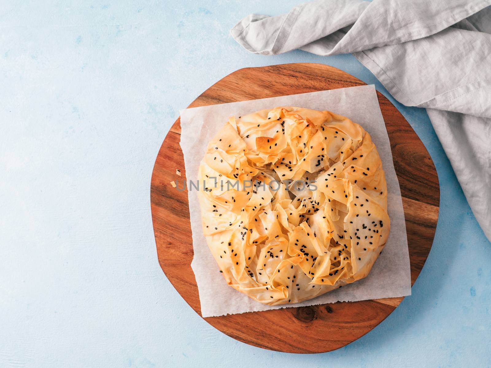 Greek pie spanakopita on white baking paper over blue background. Vegetarian or vegan Spanakopita Spinach Pie from fillo pastry. Copy space. Ideas and recipes for healthy lunch. Top view or flat lay.