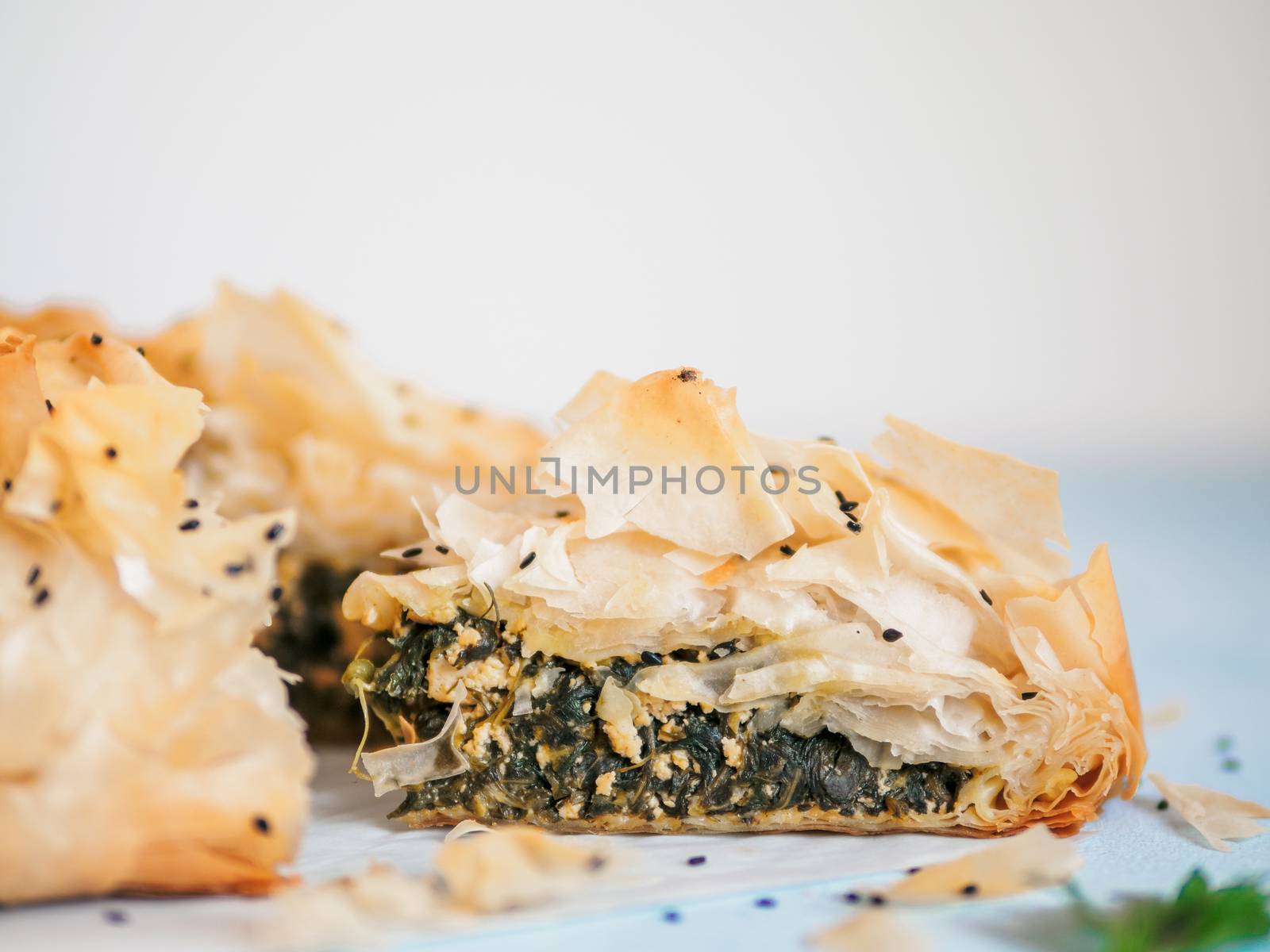 Greek pie spanakopita on blue table with shallow DOF. Slice of vegetarian or vegan Spanakopita Spinach Pie with copy space. Ideas and recipes for healthy lunch.