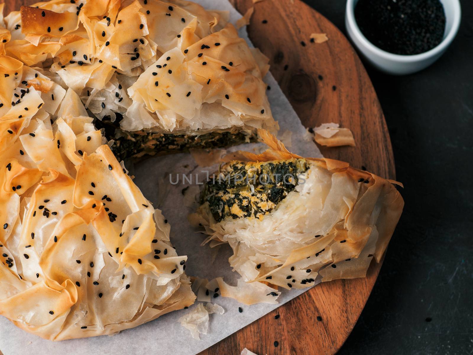 Greek pie spanakopita on dark background. Ideas and recipes for vegetarian or vegan Spanakopita Spinach Pie from fillo pastry cut in slices. Copy space. Top view or flat lay.