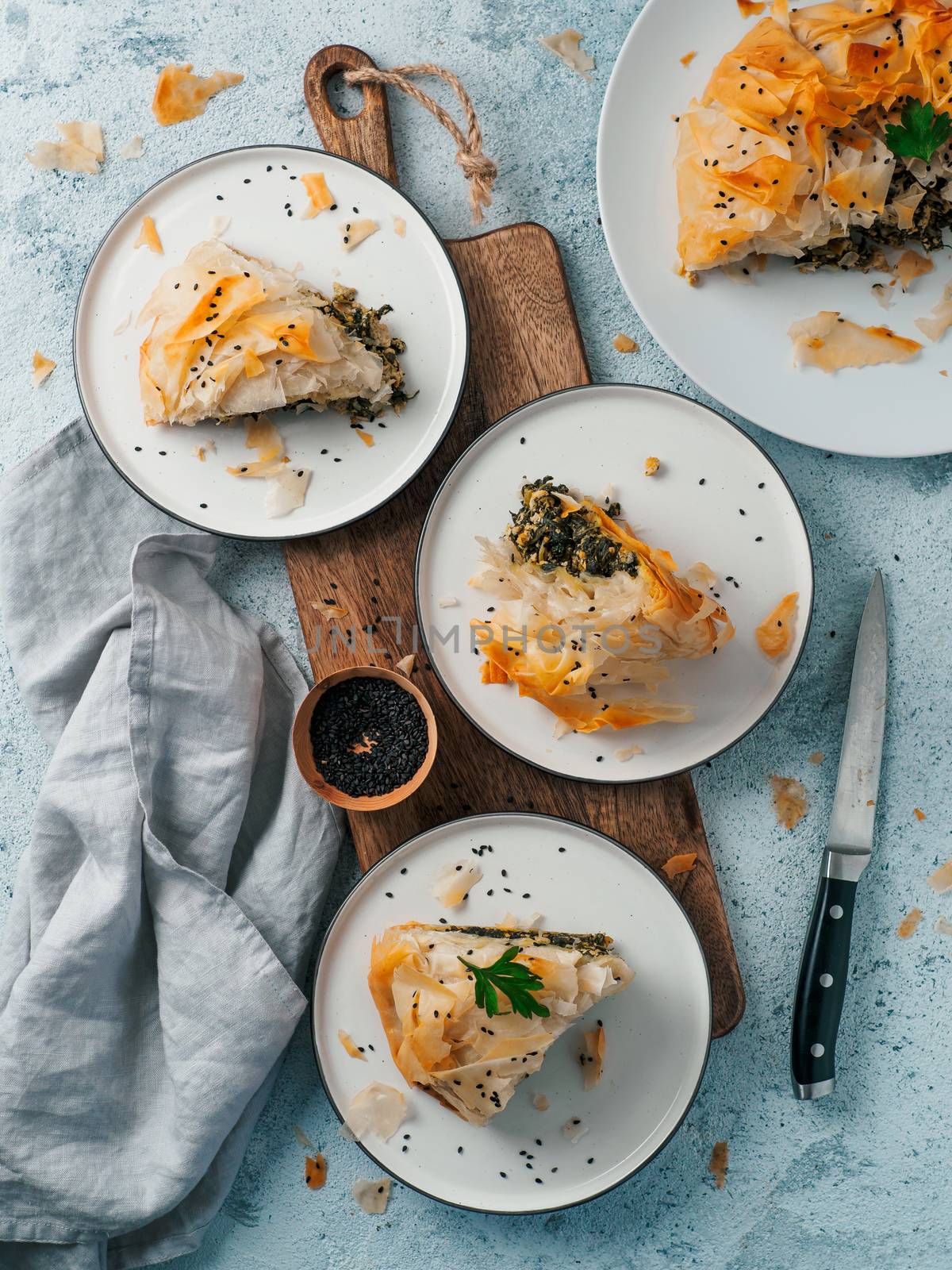 Greek pie spanakopita on gray background. Ideas and recipes for vegetarian or vegan Spanakopita Spinach Pie from fillo pastry. Slices pie on plates. Copy space. Top view or flat lay. Vertical.