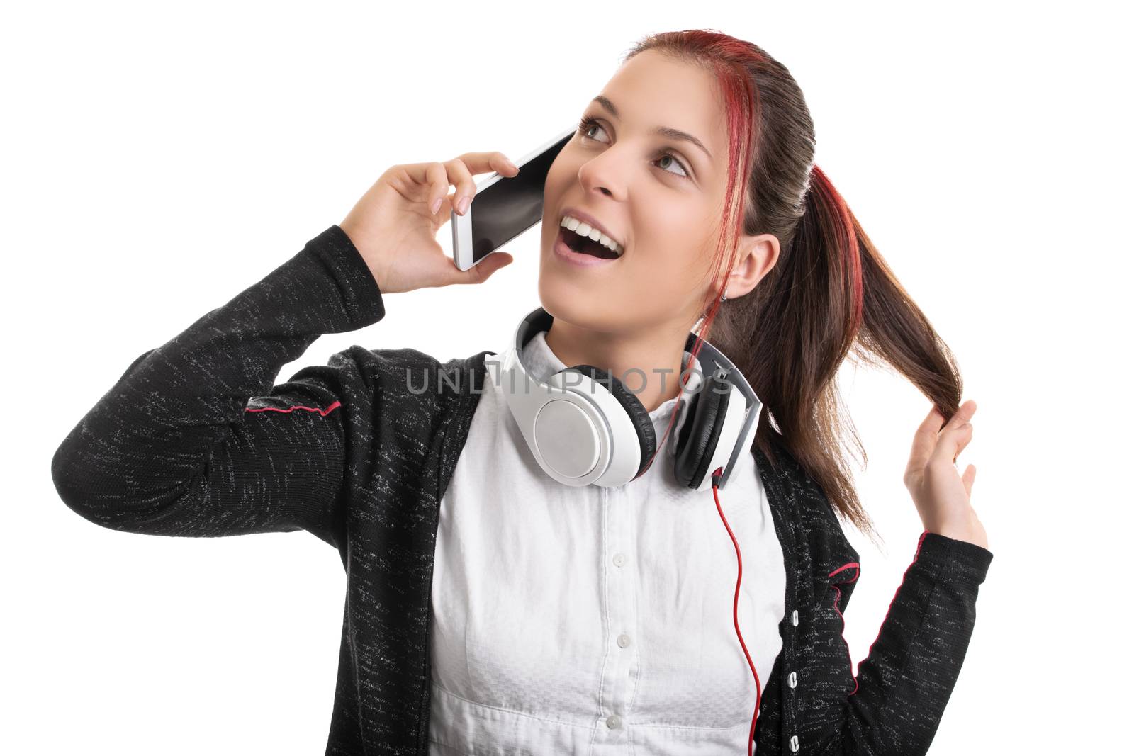 Close up shot of a beautiful smiling young girl in uniform with headphones around her neck, talking on the phone and playing with her hair, isolated on white background.