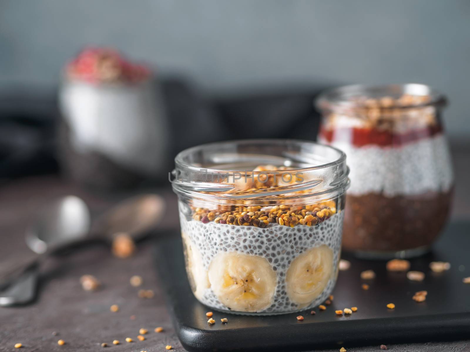 Healthy breakfast concept and idea - chia pudding with organic banana, oatmeal granola and bee pollen. Glass jar with chia seeds puding on dark table. Copy space for text