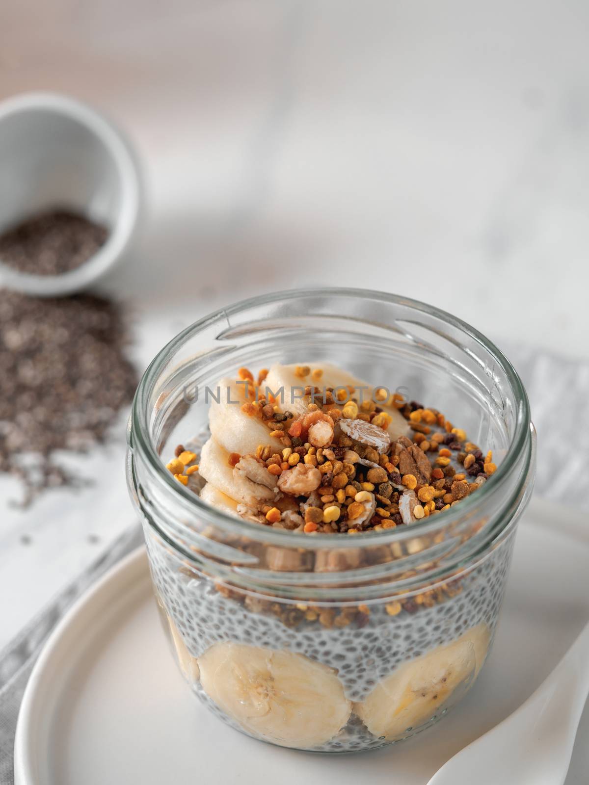 Healthy breakfast concept and idea - chia pudding with organic banana and bee pollen. Glass jar chia puding on white marble table. Copy space for text