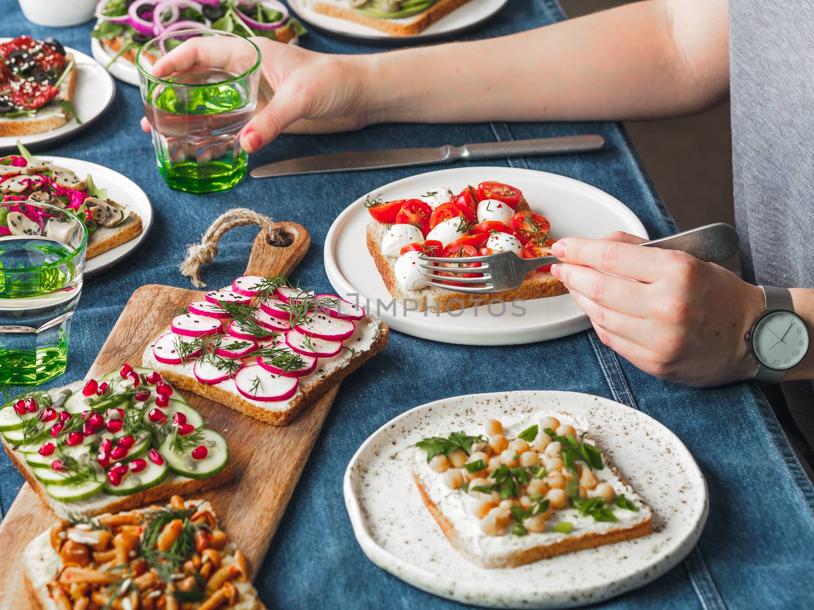 Female hands on dinning table. Young woman eat vegetarian toast. Vegan veggies sandwiches on dinning table