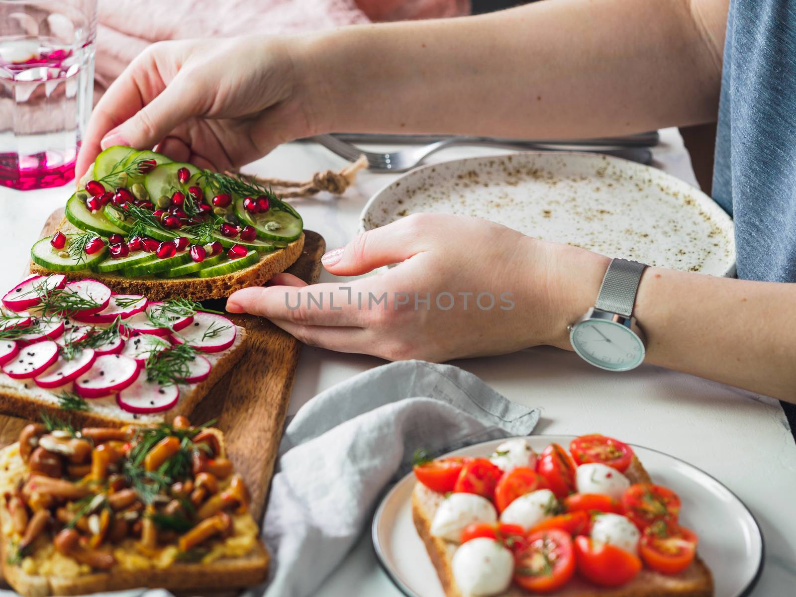 Female hands on dinning table. Young woman eat vegetarian toast. Vegan veggies sandwiches on dinning table