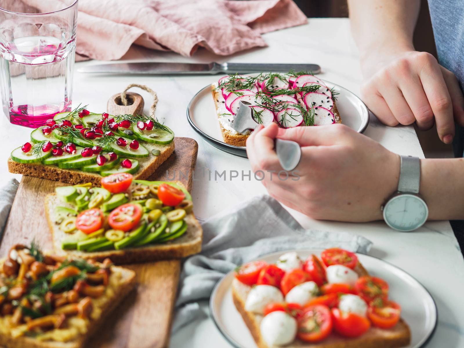 Female hands on dinning table. Young woman eat vegetarian toast. Vegan veggies sandwiches on dinning table