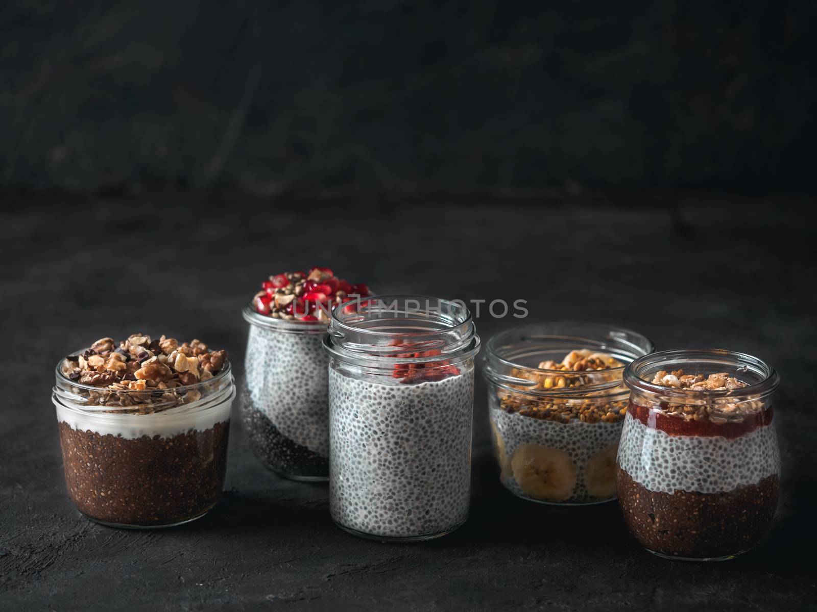 Set of chia pudding in different glass jars on dark table. Assortment of chia puding with different fruits, nuts,ingredients. Copy space for text. Superfood,detox,healthy overnight breakfast concept