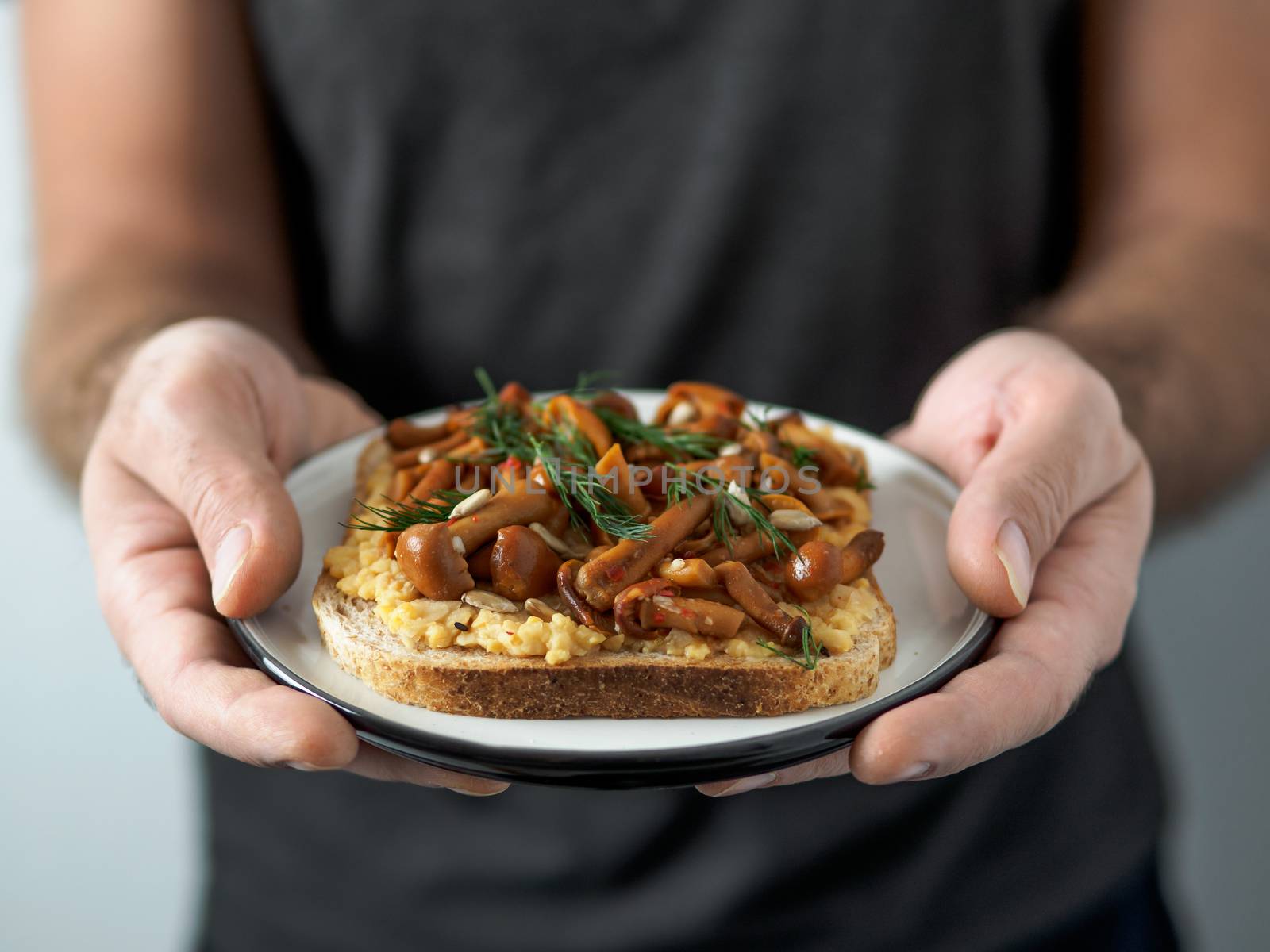 Hands takes plate with vegan sandwich. Healthy appetiezer - whole wheat bread toast with chickpea hummus and honey fungus mushrooms