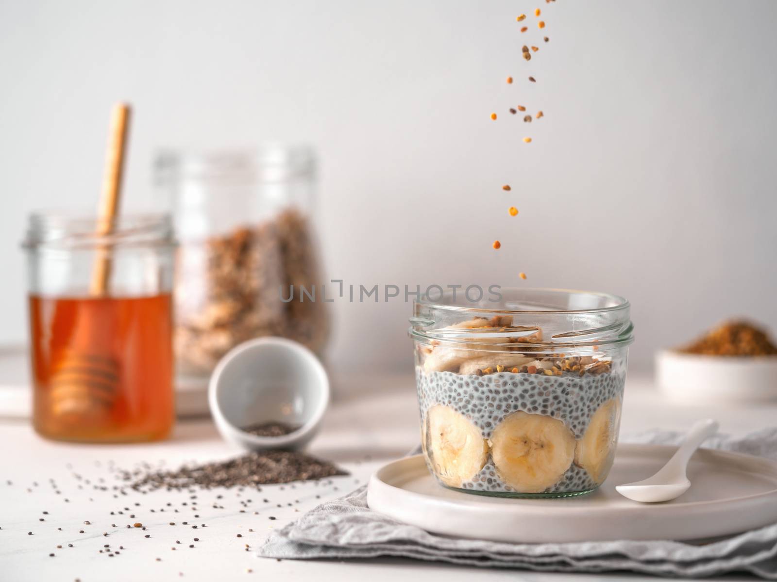 Healthy breakfast concept and idea - chia pudding with organic banana and oatmeal granola.Glass jar with falling oatmeal on white table.Copy space