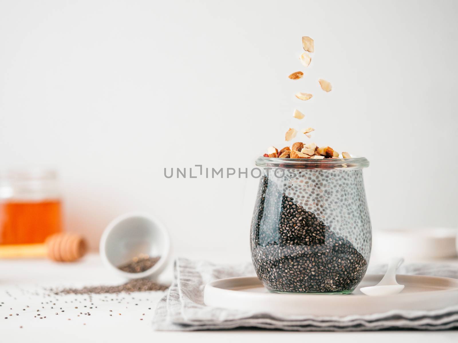 Healthy breakfast concept and idea - two colors chia pudding with organic raw almond. Glass jar with black charcoal and white vegan milk chia pudding with falling chopped almond. Copy space