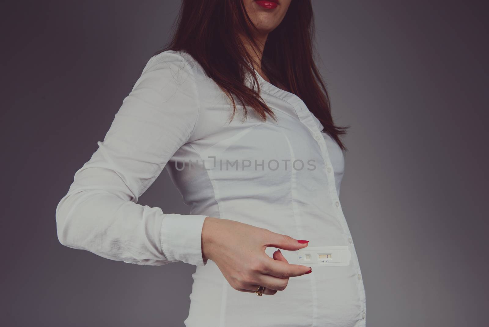 Young woman checking pregnancy test with positive result. Studio shoot.