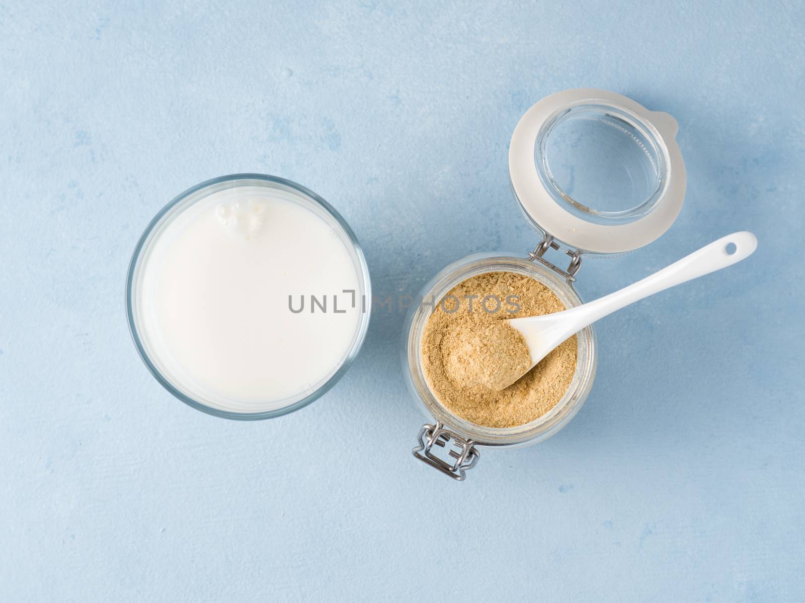 Nutritional yeast and milk. Nutritional inactive yeast in jar and glass of milk on blue tabletop. Copy space. Top view. Nutritional yeast is vegetarian superfood with cheese flavor, for healthy diet
