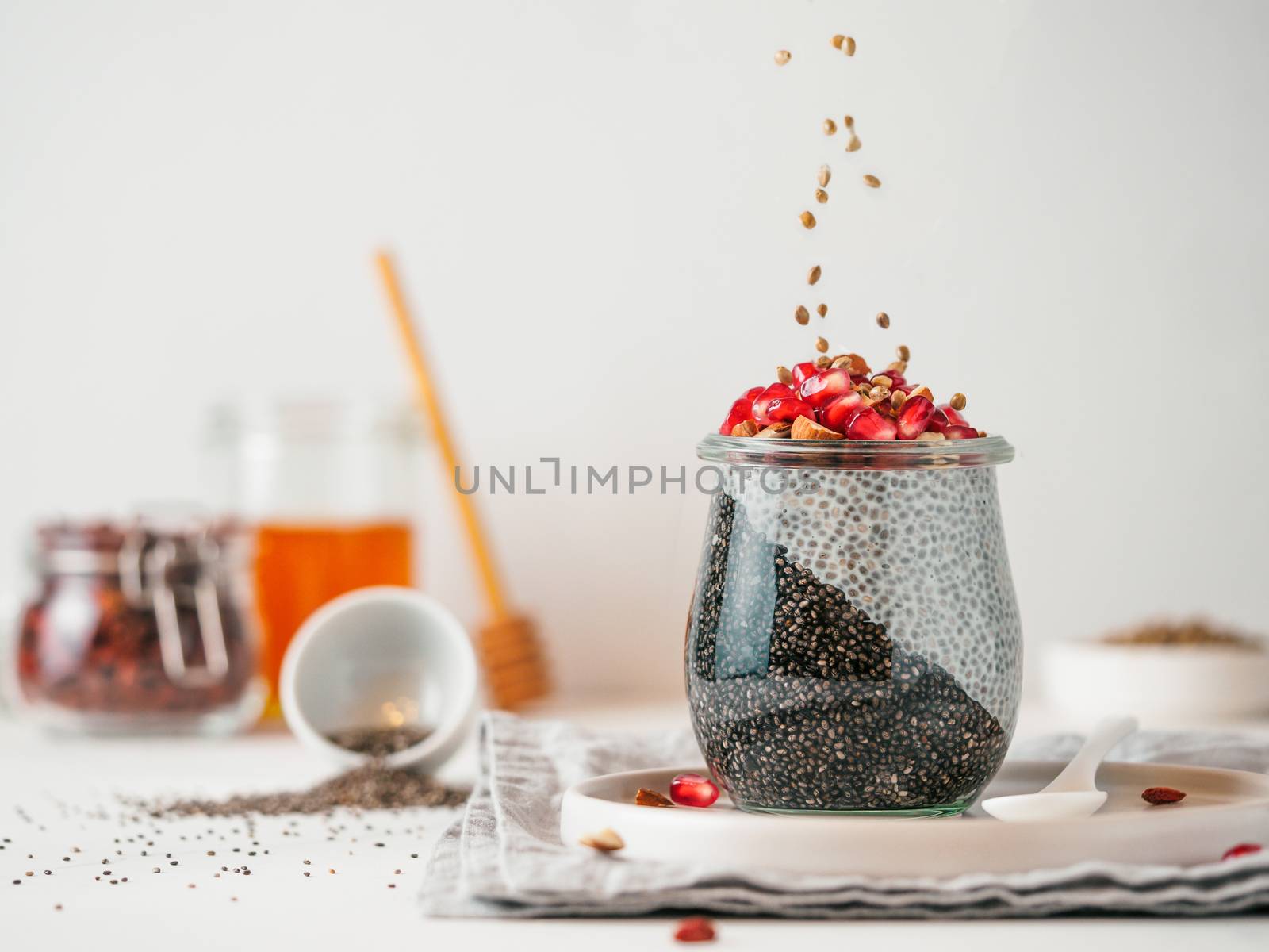 Healthy breakfast concept and idea - two colors chia pudding with organic raw pomegranate. Glass jar with black charcoal and white vegan milk chia pudding with falling hemp seed. Copy space