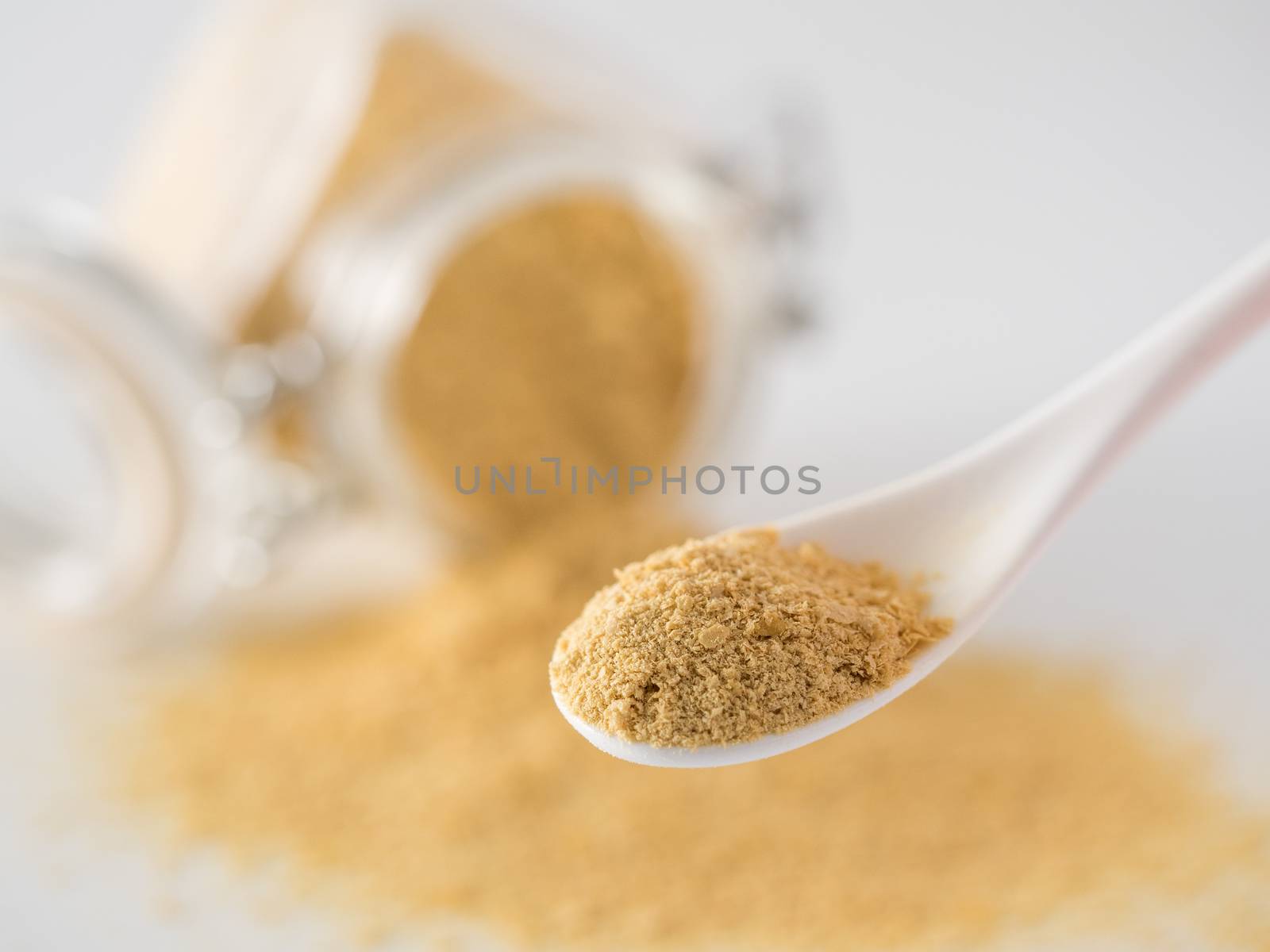 Nutritional yeast background. Nutritional inactive yeast in small spoon and spilled from glass jar on background. Copy space. Nutritional yeast is vegetarian superfood with cheese flavor