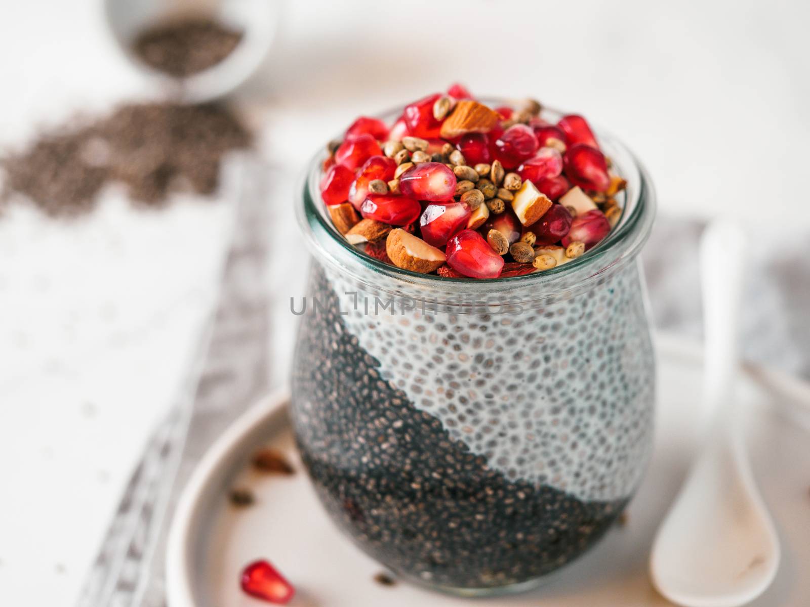 Healthy breakfast concept and idea - two colors chia pudding with organic raw pomegranate, almond and hemp grains. Glass jar with black charcoal and white vegan milk chia pudding. Copy space for text