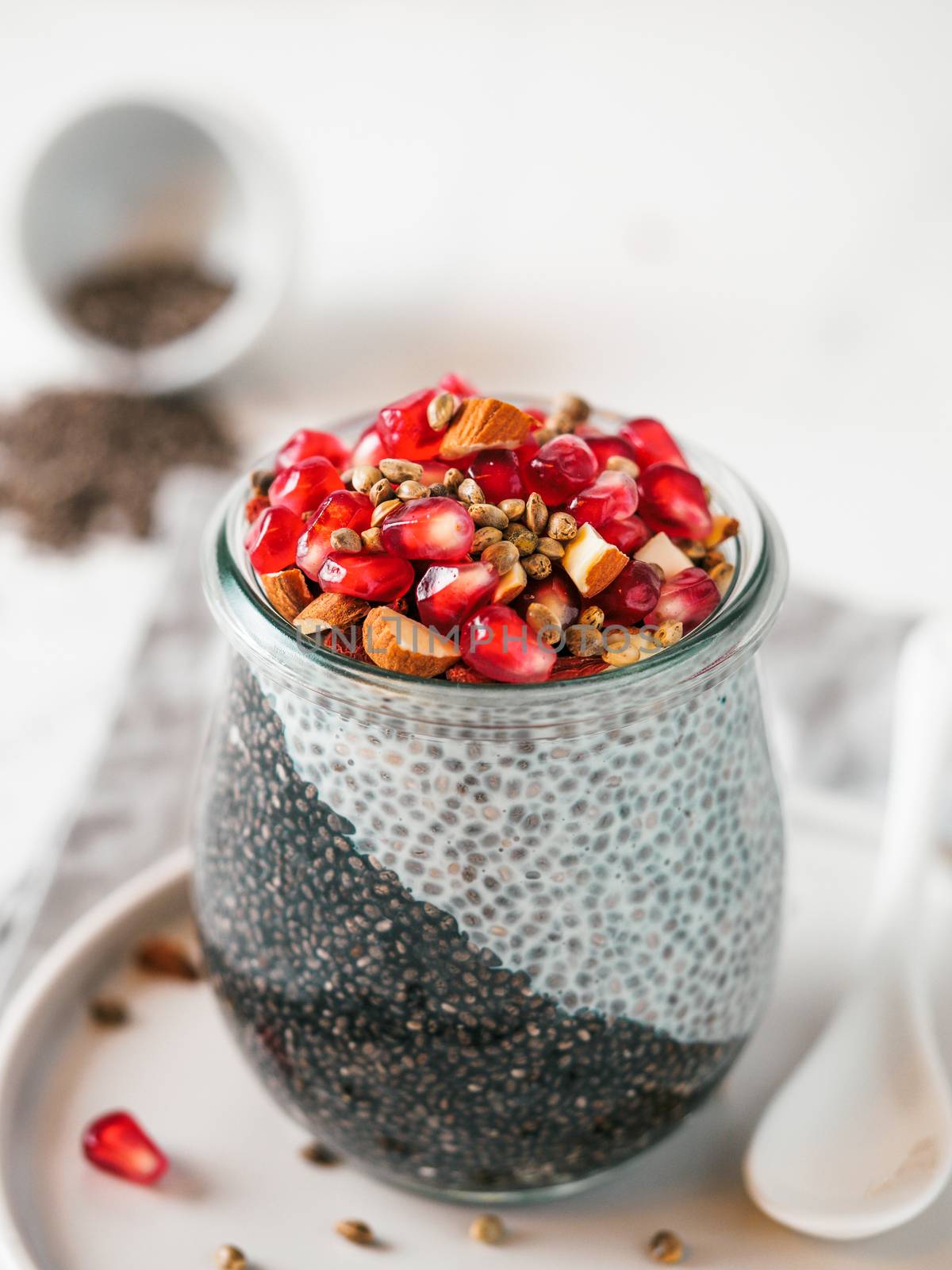 Healthy breakfast concept and idea - two colors chia pudding with organic raw pomegranate, almond and hemp grains. Glass jar with black charcoal and white vegan milk chia pudding. Copy space. Vertical