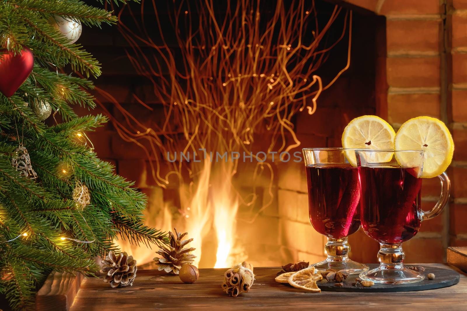 Christmas composition - two glasses with mulled wine on a wooden table near a Christmas tree opposite a burning fireplace.