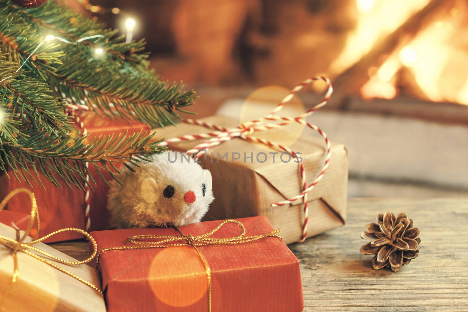 Christmas composition - mouse is symbol of 2020 according to Chinese horoscope next to gifts under Christmas tree in room by fireplace by galsand