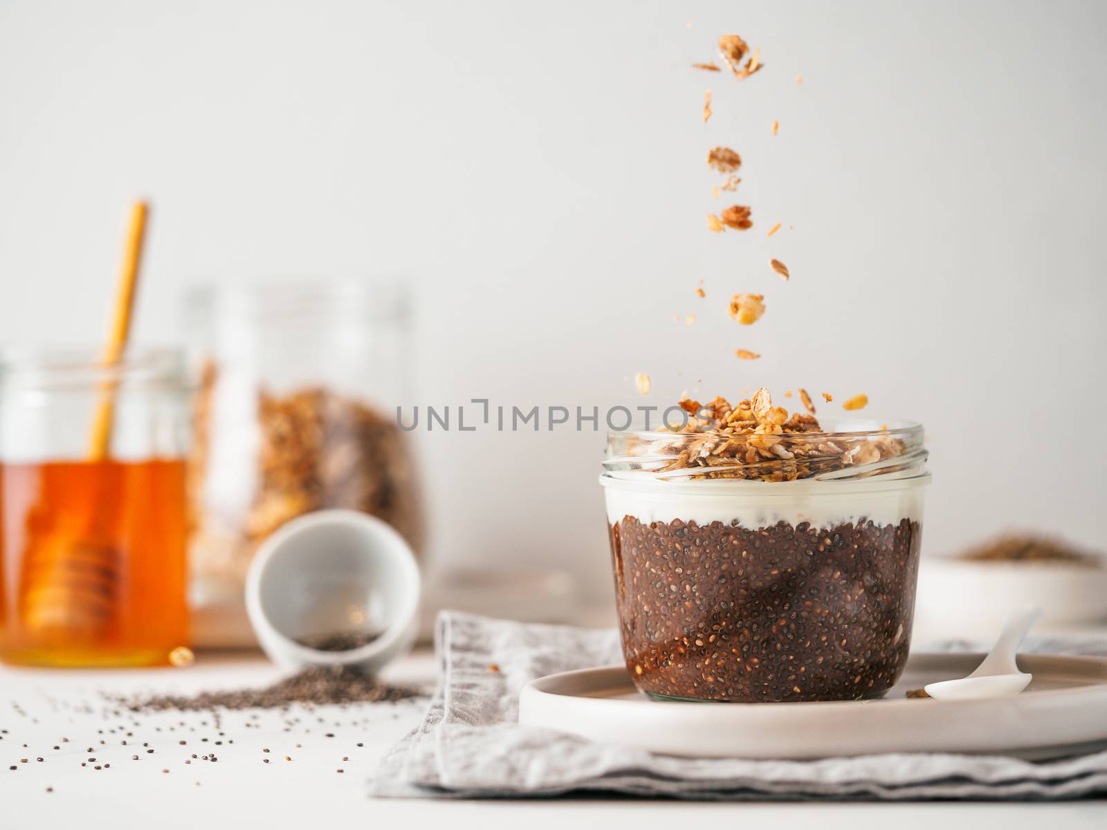 Healthy breakfast concept and idea- chia pudding with organic raw cocoa,white vegan soft cheese and oatmeal granola.Glass jar with chocolate chia pudding with falling oatmeal on white table.Copy space