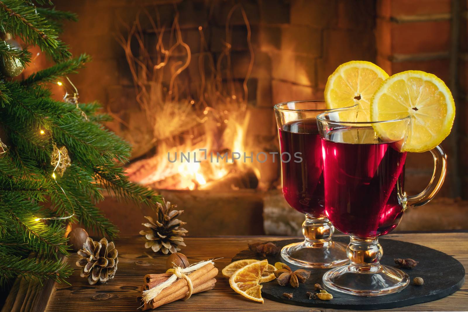 Christmas composition - two glasses with mulled wine on a wooden table near a Christmas tree opposite a burning fireplace.