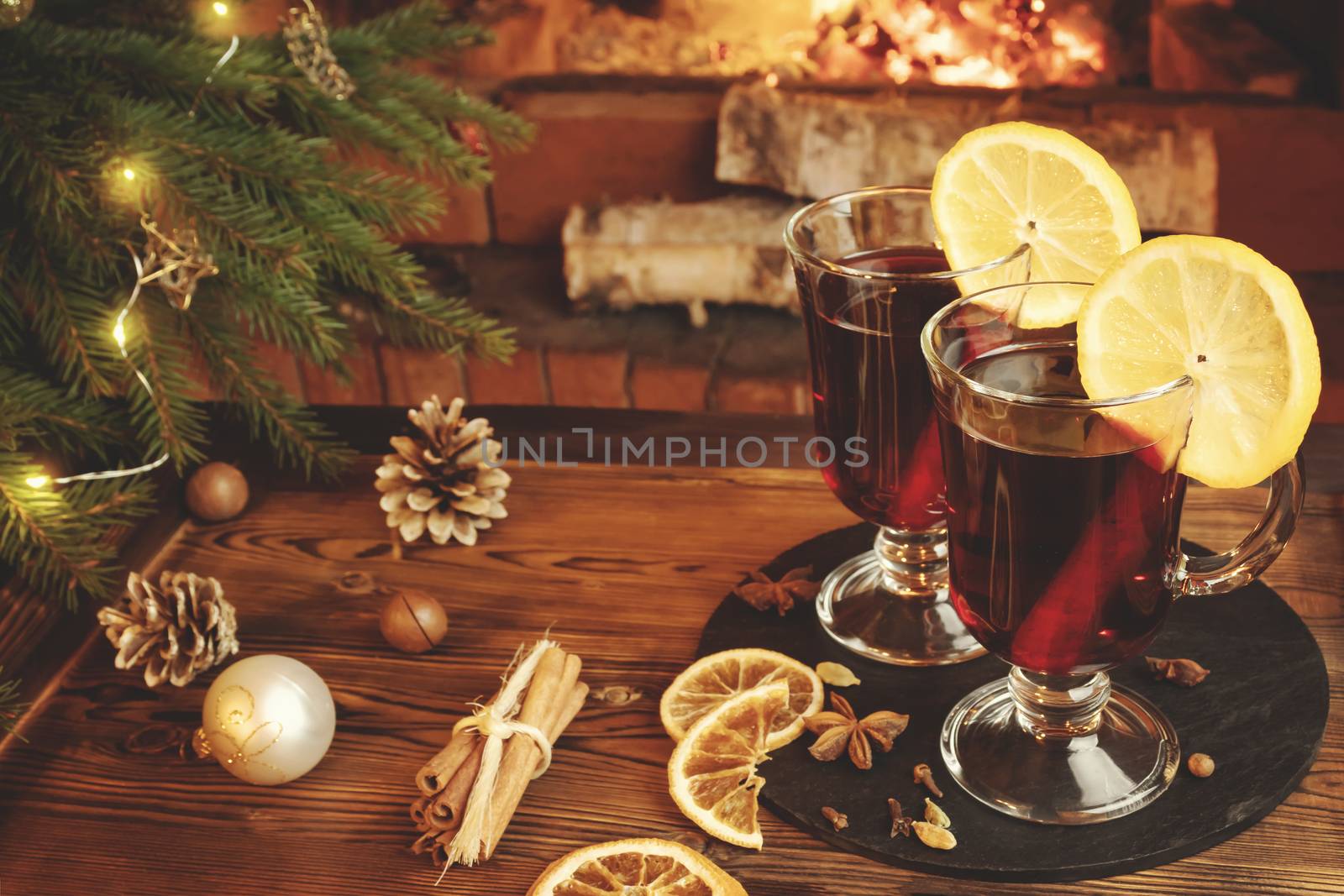 Christmas composition - two glasses with mulled wine on a wooden table near a Christmas tree opposite a burning fireplace.