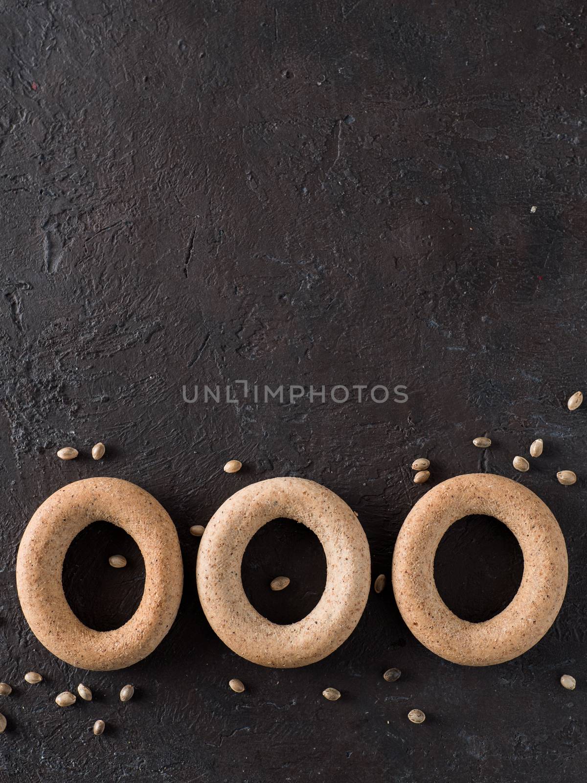 Ring-shaped cracknel with whole grain hemp seed flour and hemp seeds on black background. ring-shaped cracknel close up. Copy space Top view or flat lay. Vertical.