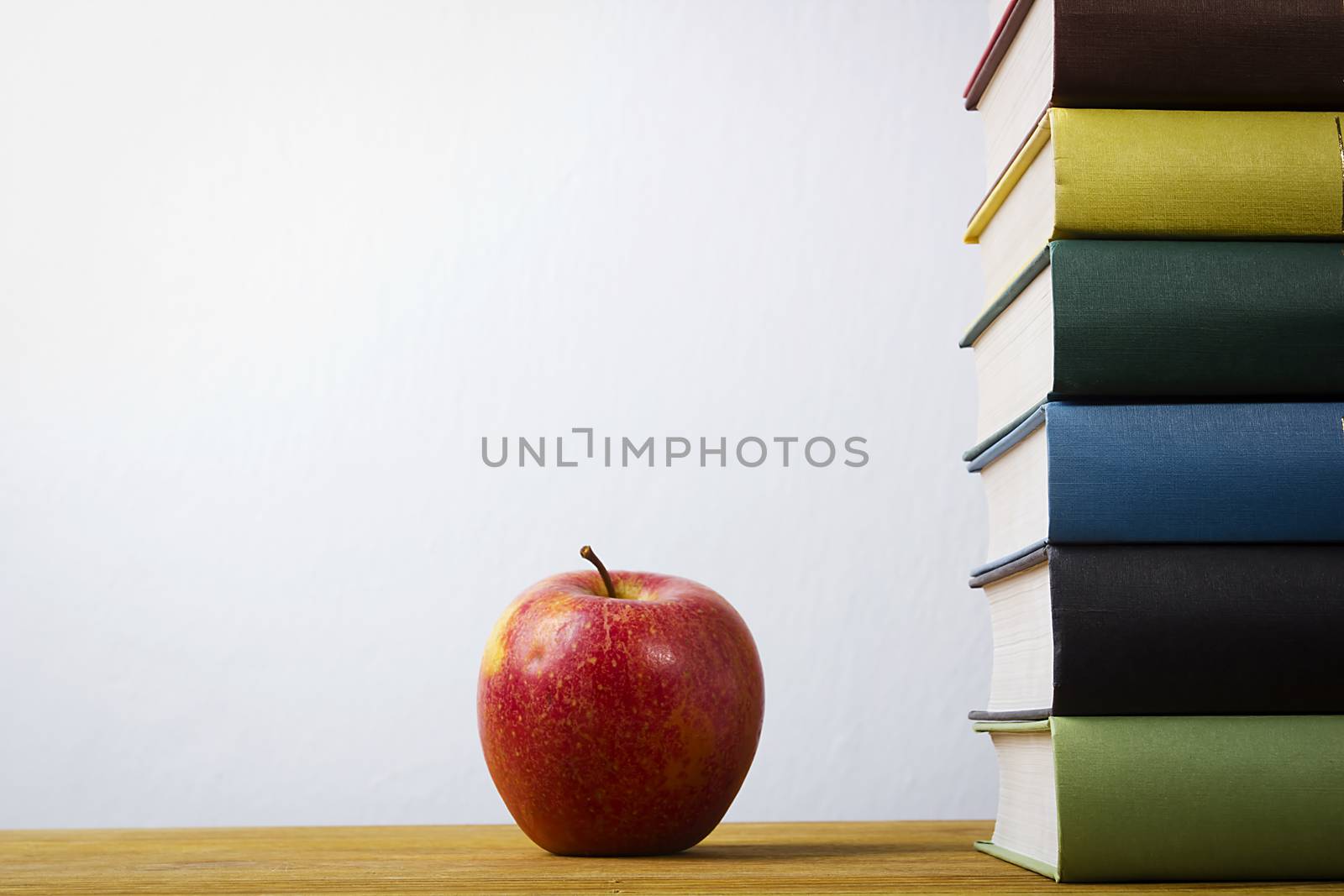 Stack of books with multi-colored binders and an apple on a wooden table