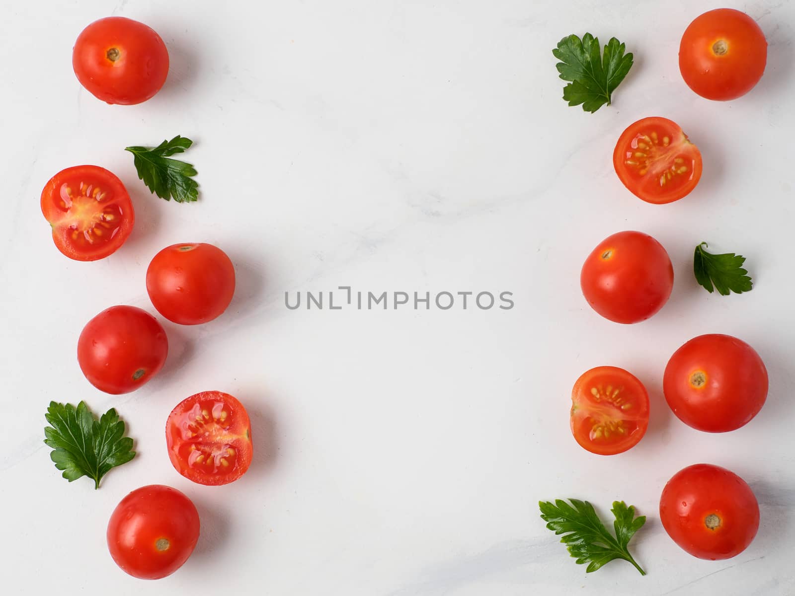 Orange tomatoes on white marble table. Small red cherry tomatoes with half sliced tomato and fresh parsley leaves. Top view or flat lay. Copy space for text.