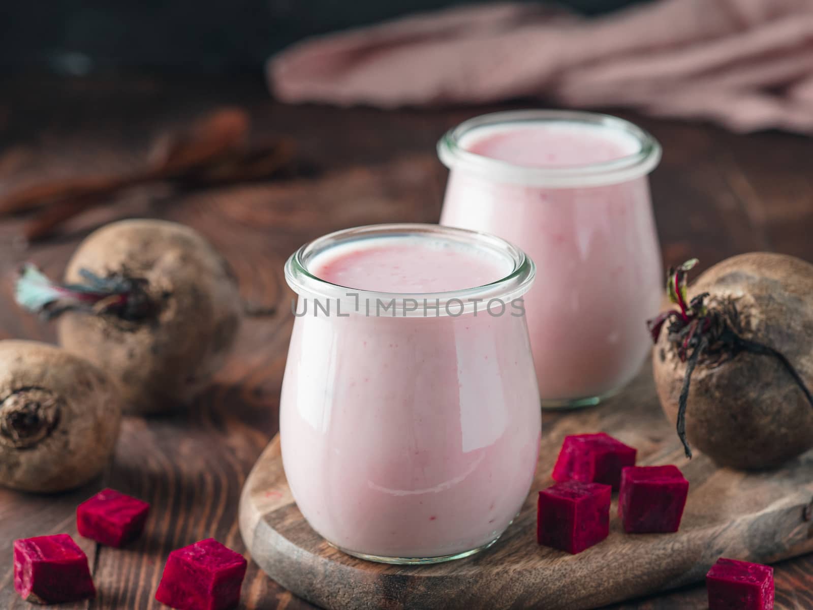 Yogurt with beetroot. Two glass jar with pink yoghurt or milkshake and red beetroot on wooden cutting board over dark background. Copy space for text.