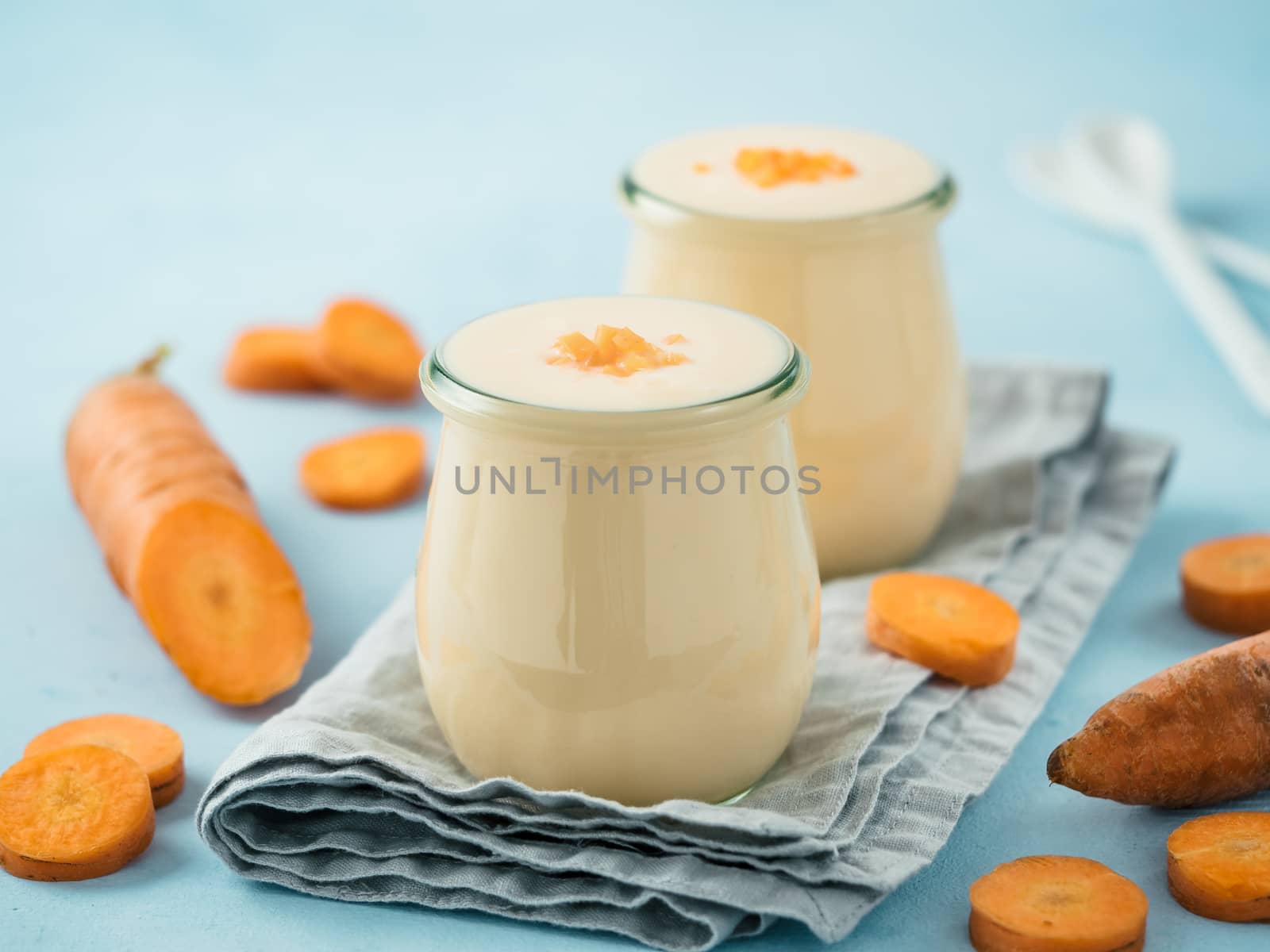 Yogurt with carrot. Vegetable yogurt. Two glass jar with yellow orange yoghurt or milkshake and fresh carrot on blue background. Copy space for text