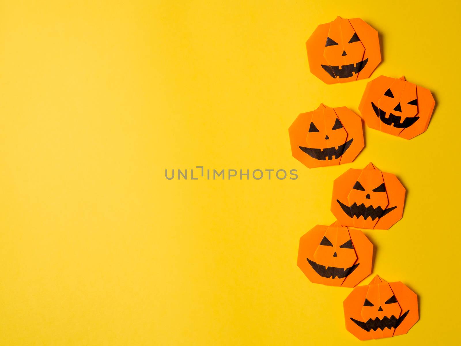 Halloween concept. Paper origami pumpkin on yellow background. Simple idea for halloween - easy made paper pumpkins on trendy color Ceylon Yellow background. Copy space for text.