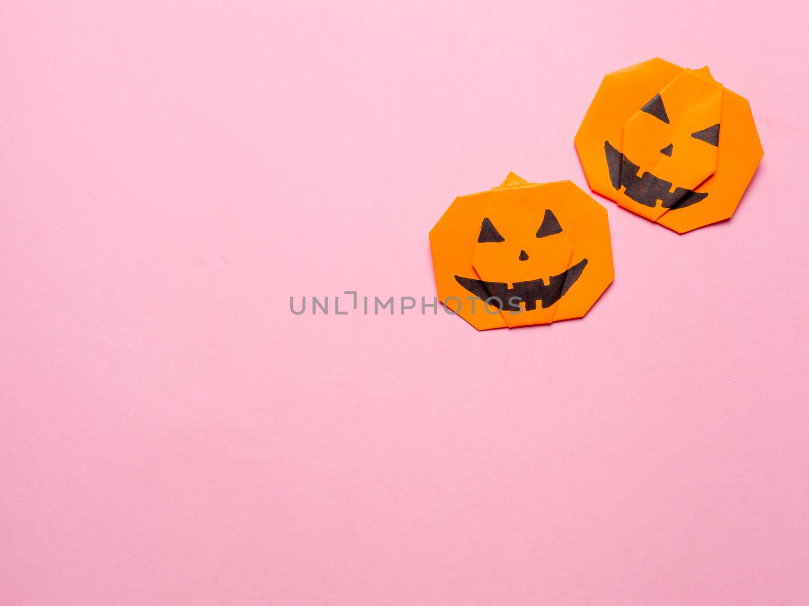 Halloween concept. Paper origami pumpkin on pink background. Simple idea for halloween - easy made paper pumpkins on trendy color Ceylon Yellow background. Copy space for text.
