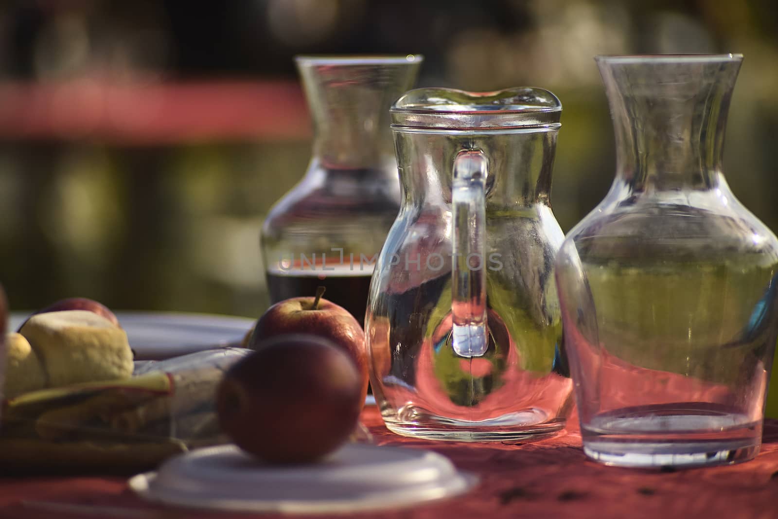 A table set in a Venetian tavern, featuring wine glasses, apples and breads in the foreground, all ready to serve lunch. Image with a predominant red color contrasting with the transparency of the glass of the carafe.
