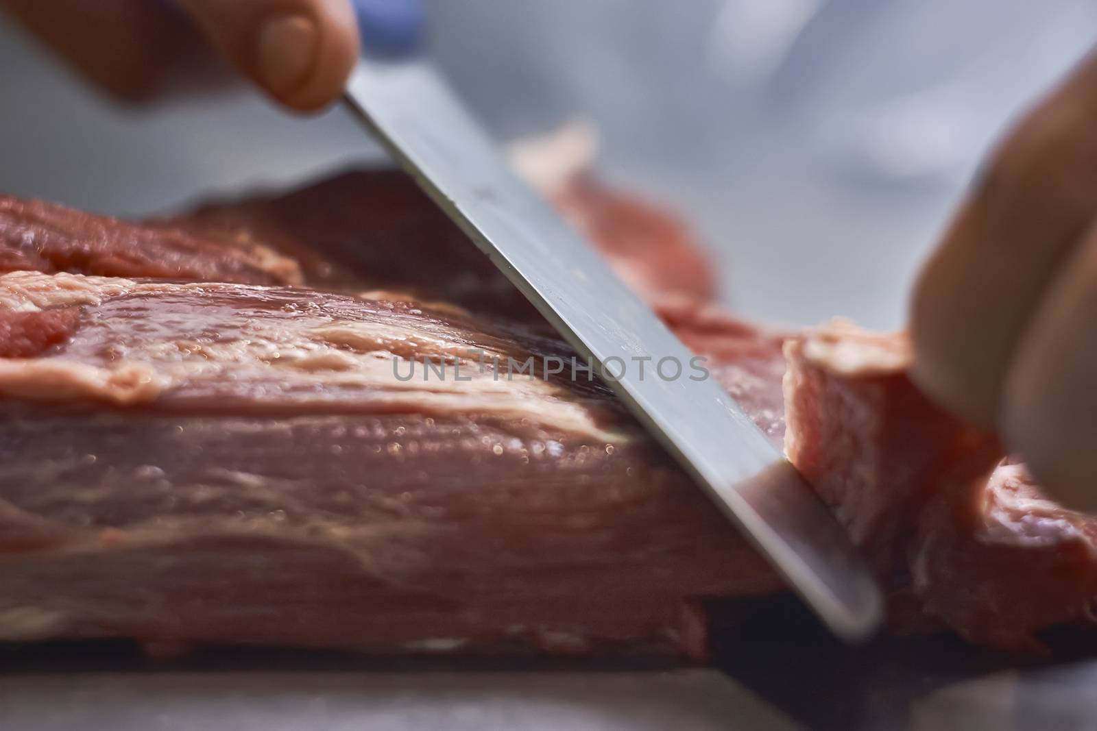 butcher who using a knife is slicing the meat in order to be sold and later eaten in his butcher's shop.