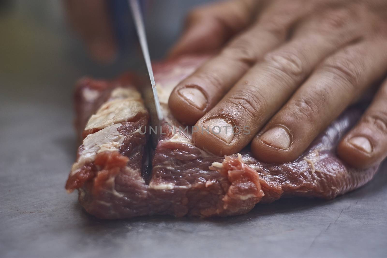 detail of the hand of a butcher intending to cut a piece of meat with the knife of which you notice very well the fibers and texture,