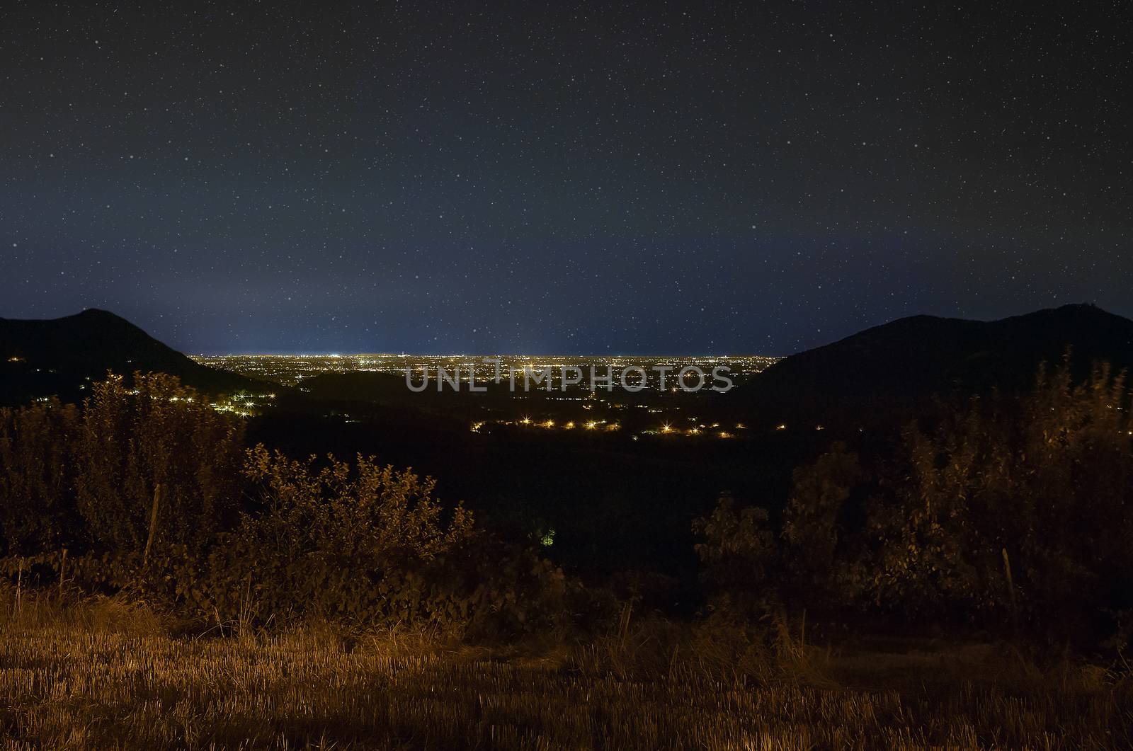 Hilly landscape of northern Italy, Precisely of Este in Veneto. Very impressive night landscape where you can see the hills at the sides and the lights of the city that are lost in the sky below a starry sky.