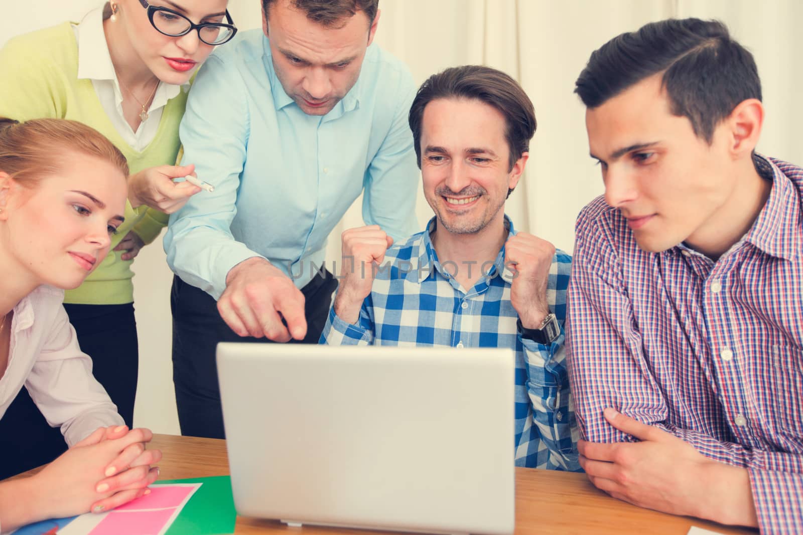 Business team cheering with thumbs up looking at one laptop at workplace