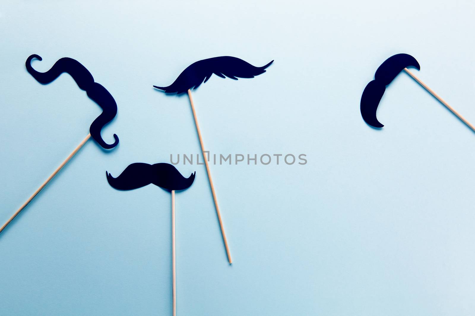 Group of accessories in form of black moustaches on sticks on grey blue background with copy space. Concept men's health, prostate cancer awareness month, charity, Father's Day. Flatlay.