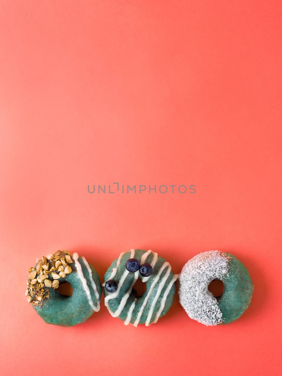 Color of year 2019 Living Coral concept. Spirulina glaze donuts on coral paper background. Top view or flat lay. Copy space for text. Vertical.